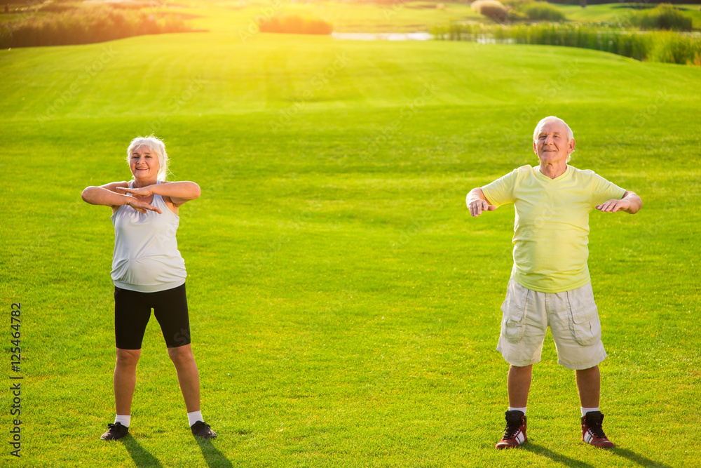 Obraz premium Senior couple exercising. Smiling people on meadow background. Keep working on yourself. Result is worth it.