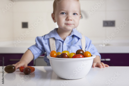 Baby boy playing with ripe colorful cherry tomatoes