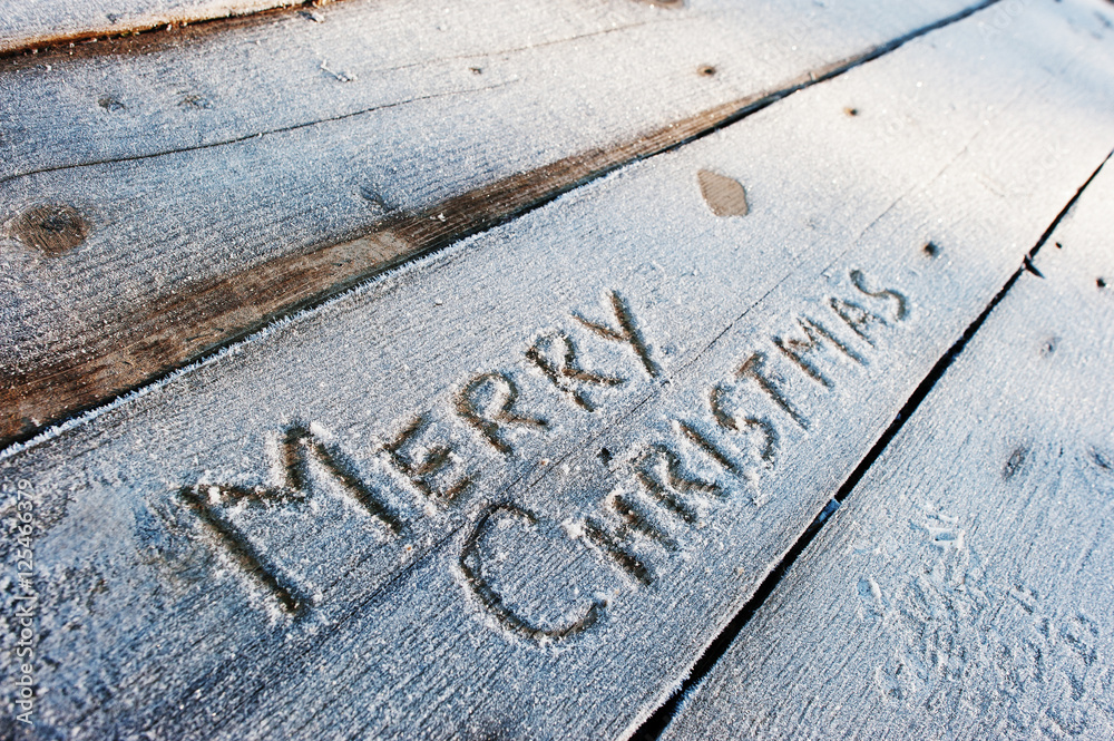 Merry Christmas written on a wooden background with frosts