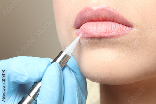 Cosmetologist making permanent  make up on lips, close up
