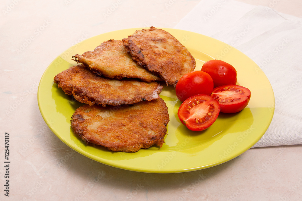 Potato pancakes with meat and tomatoes on green plate in Belarus Potato pancakes with meat and tomatoes on green plate in Belarus