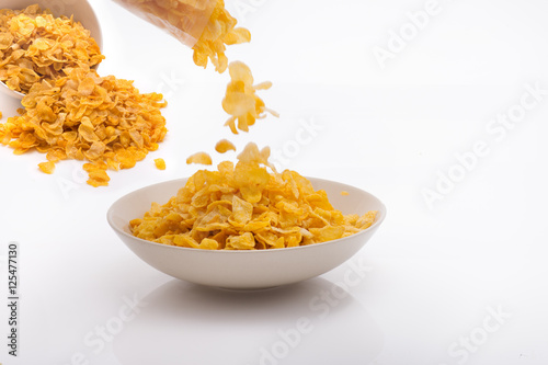 Corn Flakes being Poured into White Minimalistic Bowl Behind Spi photo