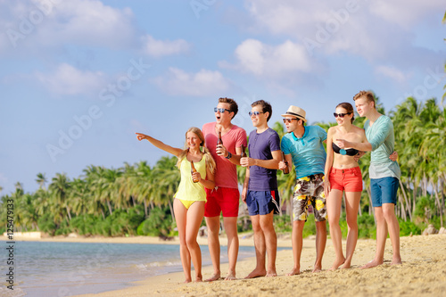 Friendship and vacation. Beach party. Group of amazed friends with bottles of beer looking and pointing away.