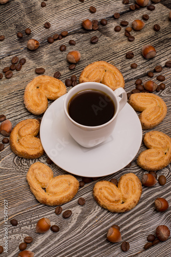 Small white cup of coffee, hazelnuts, cocoa beans, cookies on wooden background