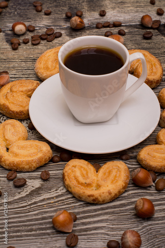 Small white cup of coffee, hazelnuts, cocoa beans, cookies on wooden background