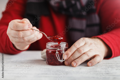 man take raspberry jam from glass jar on wooden table
