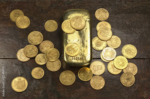 various European circulation gold coins from the 19th/20th century around a gold bar on rustic wooden background photo