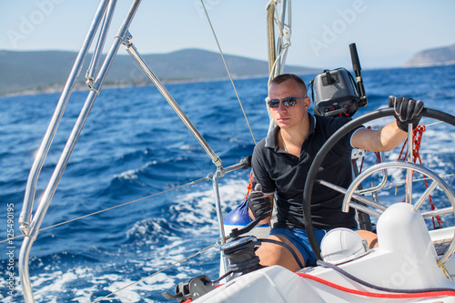 Young man steers a sailing yacht boat in the open sea.