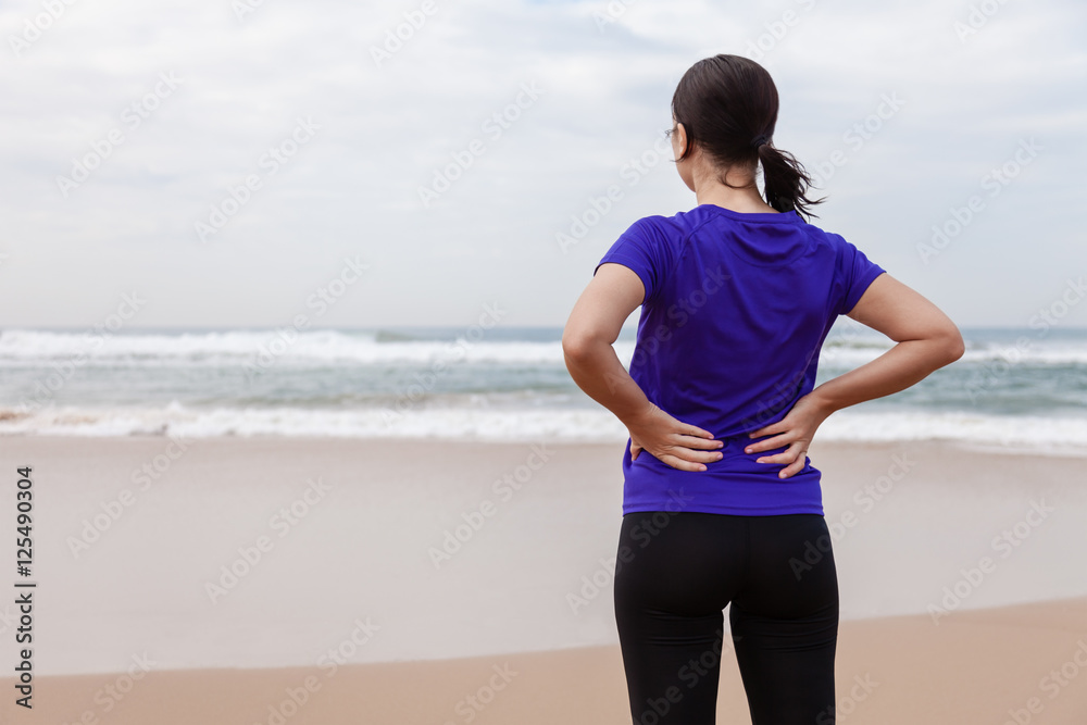 Female athlete suffering from a back injury at the beach on an Autumn day. Female athlete suffering from a back injury at the beach on an Autumn day.