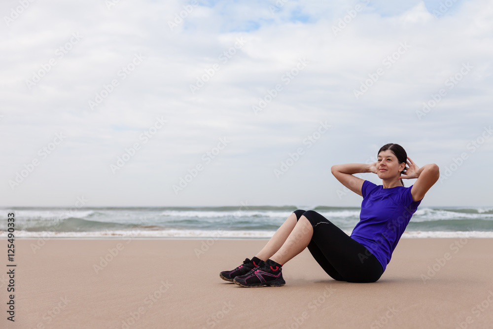 Female athlete executing situps at the beach on an Autumn day.