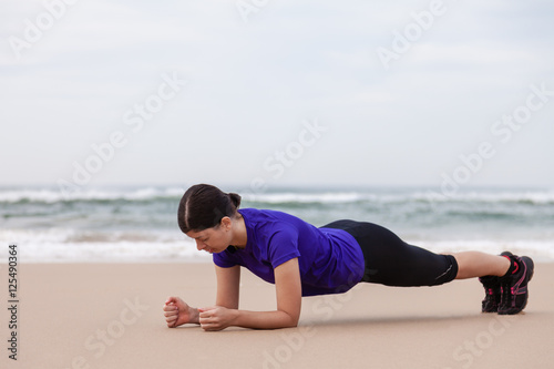 Female athlete executing the plank exercise at the beach on an Autumn day. © StockPhotosArt