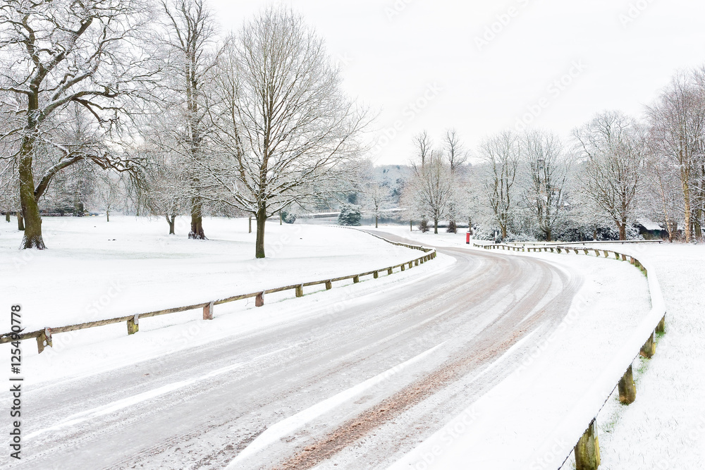 Snow on a deserted road as it curves between bare trees