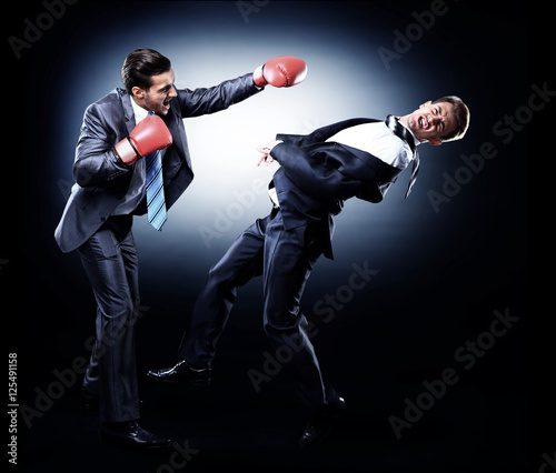 Two young businessman boxing againts dark background