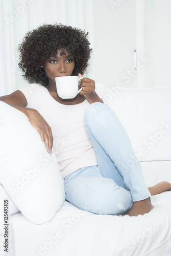 Brown skin woman sitting on white couch © apexzoom