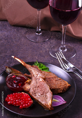 Grilled rack of lamb with pomegranate sauce in black plate on dark textural background