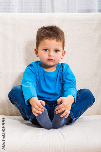 Cute little boy is sitting on sofa and thinking about something. 