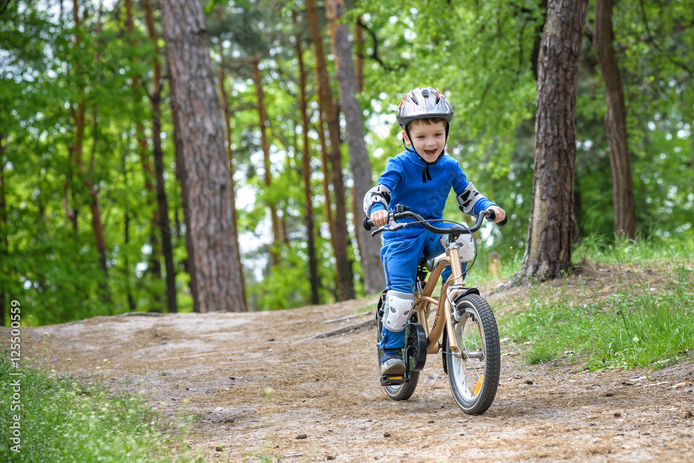 Happy funny little kid boy in colorful raincoat riding his first bike on cold day in forest. Active leisure for children outdoors. carefree childhood concept