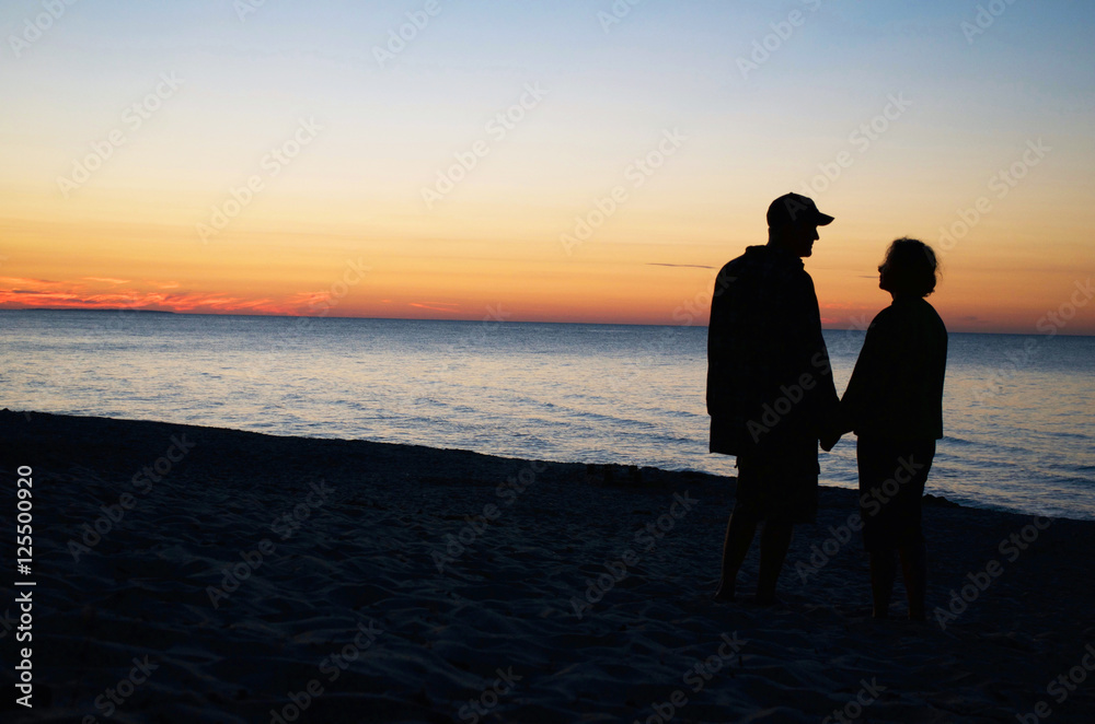 Couple holding hands at sunset on a beach.