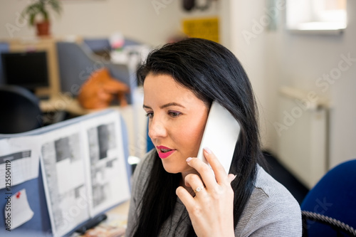 Young woman talking on mobile phone at work and advises clients