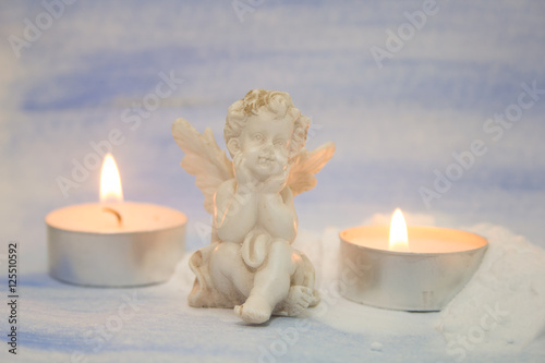 white angel figurine and candles on a pale blue background