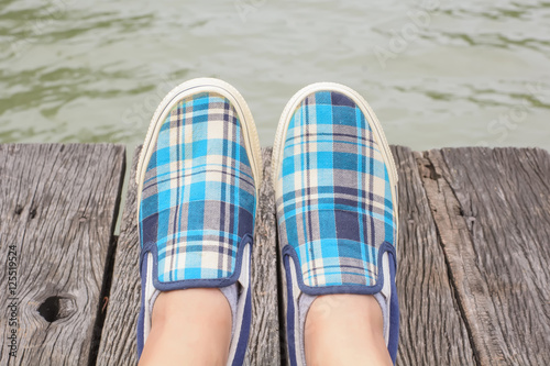 Girl wearing canvas sneakers sitting on the wooden bridge.