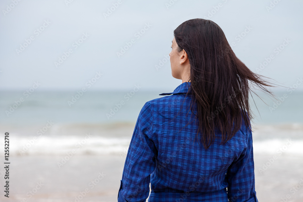 Lonely and depressed woman standing in front of the sea in a deserted beach on an Autumn day. Lonely and depressed woman standing in front of the sea in a deserted beach on an Autumn day.