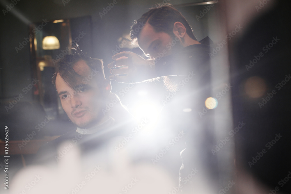 Fototapeta premium Male hairdresser cuts client with scissors in the barbershop black-and-white photo