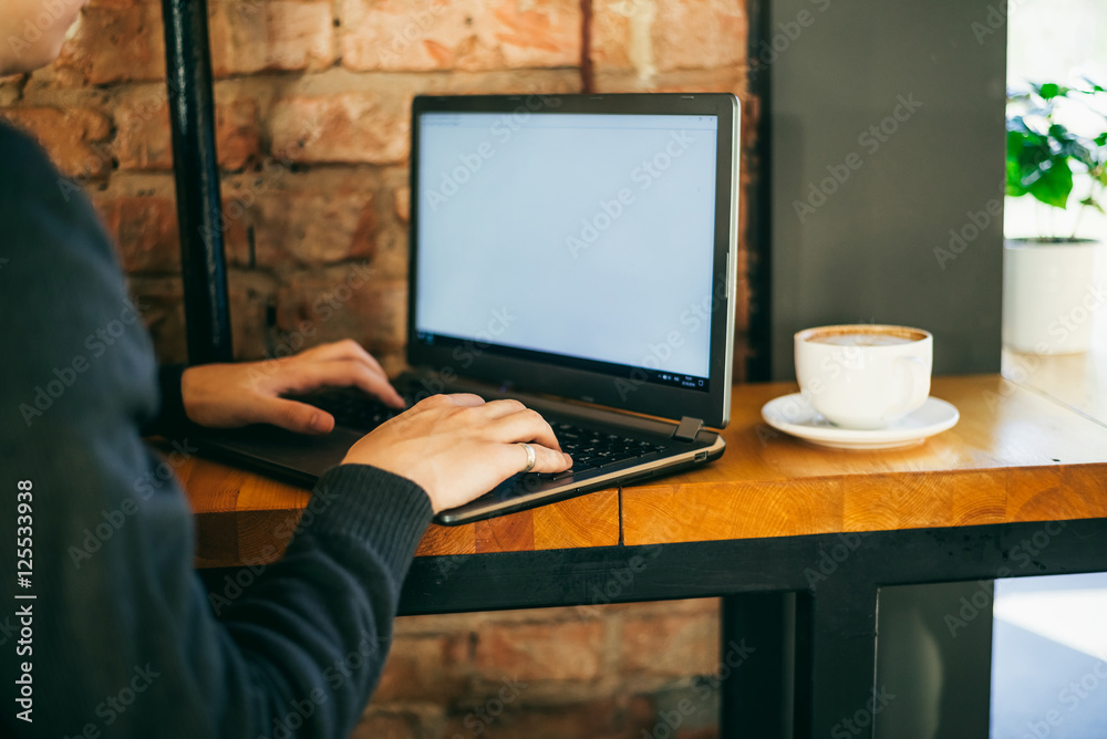 Man using, working on laptop with blank screen and drinking coffe in cafe