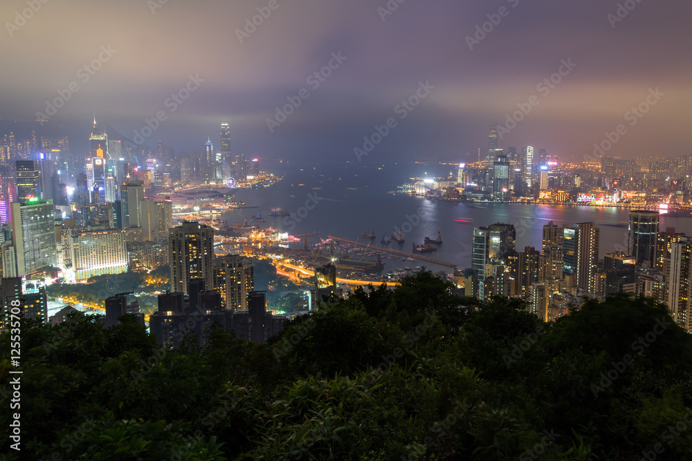 Lit skyscrapers and other buildings on Hong Kong Island and Kowloon in Hong Kong, China. Viewed from the Braemar Hill on a foggy and cloudy evening. 