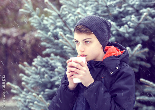 Portrait of a boy in a winter park with a paper cup of cappuccino