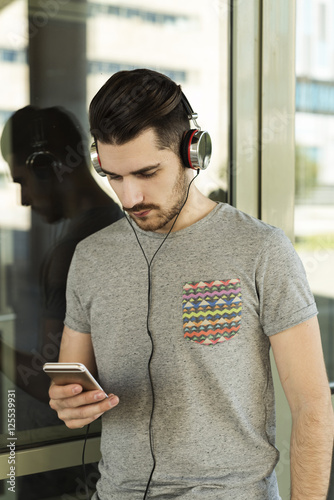 Young man using a smart phone and listening to the music with headphones
