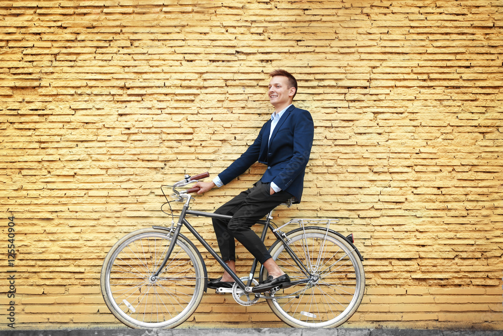 Young businessman with bicycle on yellow brick wall background Young businessman with bicycle on yellow brick wall background