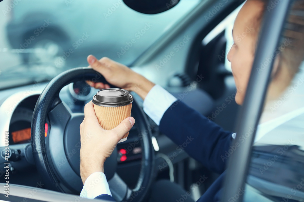 Handsome man driving a car and holding paper cup of coffee