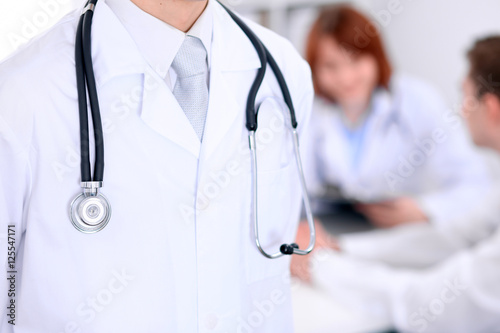 Close-up of a male doctor in a background of doctor and patient