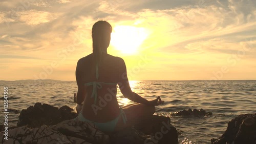 Close up tranquil girl in yoga pose on rocky ocean shore at stunning sunset photo