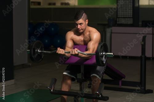 Man In The Gym Exercising Biceps With Barbell