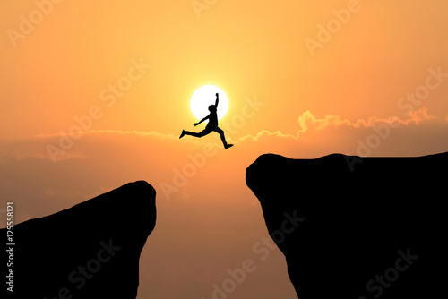 Man jump through the gap between hill.man jumping over cliff on sunset background,Business concept idea