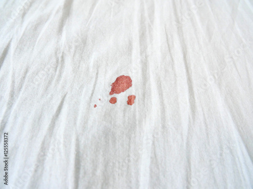 Red period spot on white bed sheet. Period stain is hard to be cleaned. Need to use hot water to wash to get rid of it.