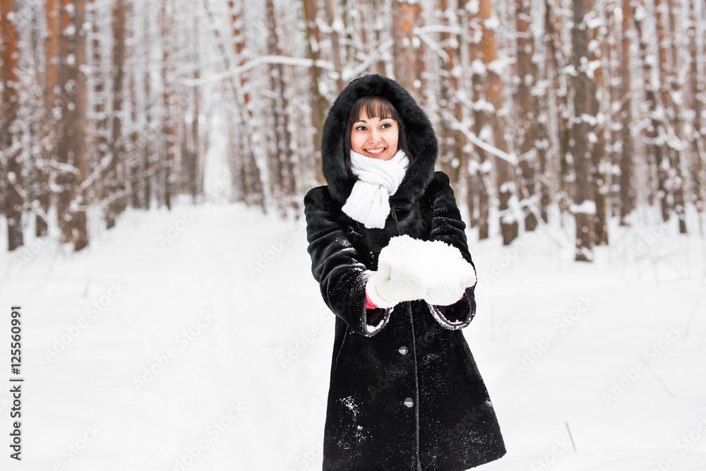 Young woman holding natural soft white snow in her hands to make a snowball, smiling during a cold winter day in the forest, outdoors. Young woman holding natural soft white snow in her hands to make a snowball, smiling during a cold winter day in the forest, outdoors.
