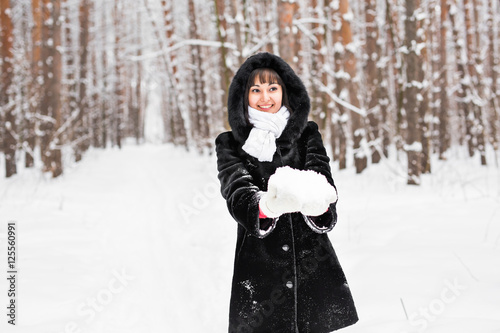 Young woman holding natural soft white snow in her hands to make a snowball, smiling during a cold winter day in the forest, outdoors. © satura_
