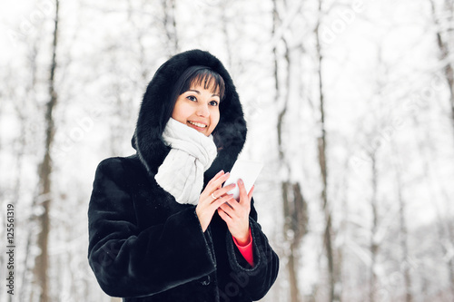 Young woman smiling with smart phone and winter landscape and snowflakes on the background