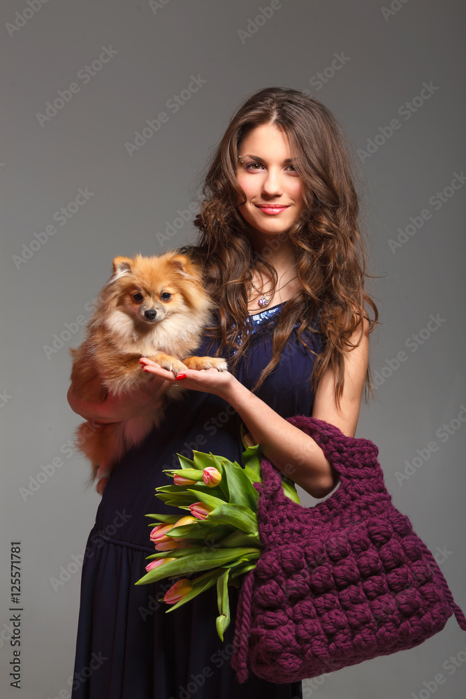 Pretty young woman with long hair holds in hands knitted bag with tulips and spitz dog Pretty young woman with long hair holds in hands knitted bag with tulips and spitz dog