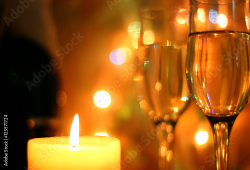 Yellow colors style Christmas greetings or New Years Eve celebration background with an elegant arrangement with flutes and bottle of champagne and burning candles. Bokeh light garland backdrops.