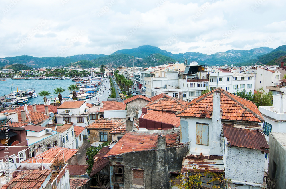 An upper view on a seaside town with old red roofs and green mountains on the background