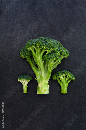 Three green broccoli on dark gray slate background