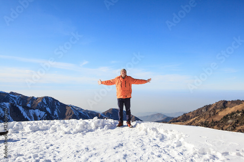 Happy man standing on the top of mountain with raised hands and enjoy. Winter travel concept 