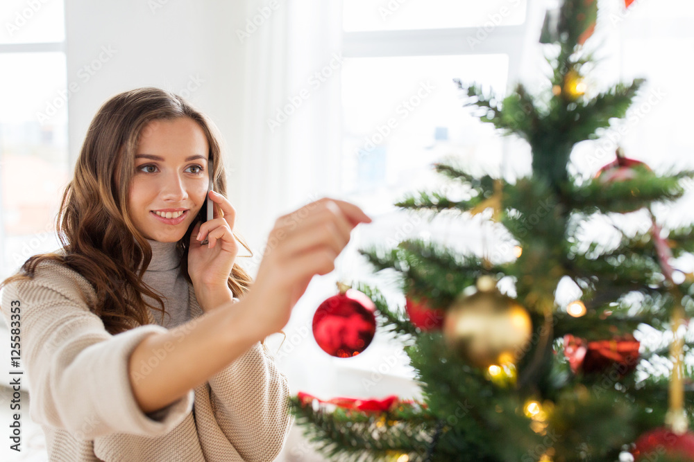 woman with smartphone decorating christmas tree
