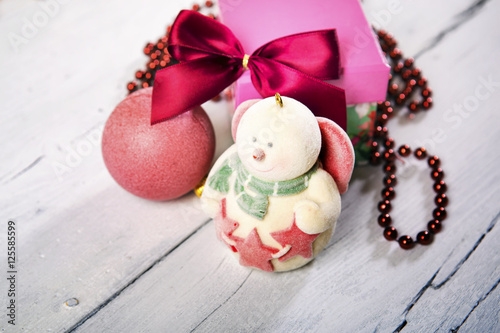 Christmas decoration. Red ball, gift, bow and snowman on white wooden background.