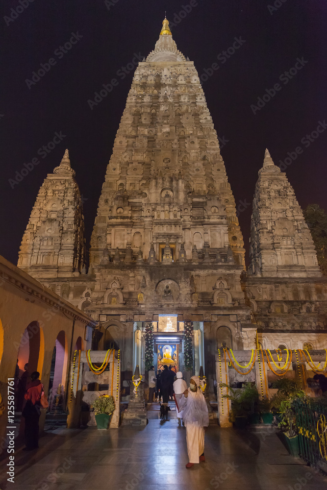 Fototapeta premium Main entrance of Mahabodhi Temple, in night-time lighting, Buddha's figure on a diamond throne, the pilgrims going to Buddha.