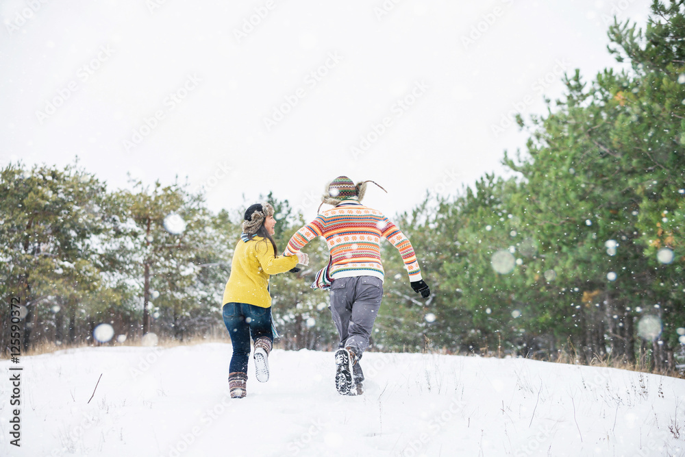 Loving couple in the winter park. Man and woman dressed in sweaters and scarves, winter hats. Snowfall in the forest, holidays, travel.